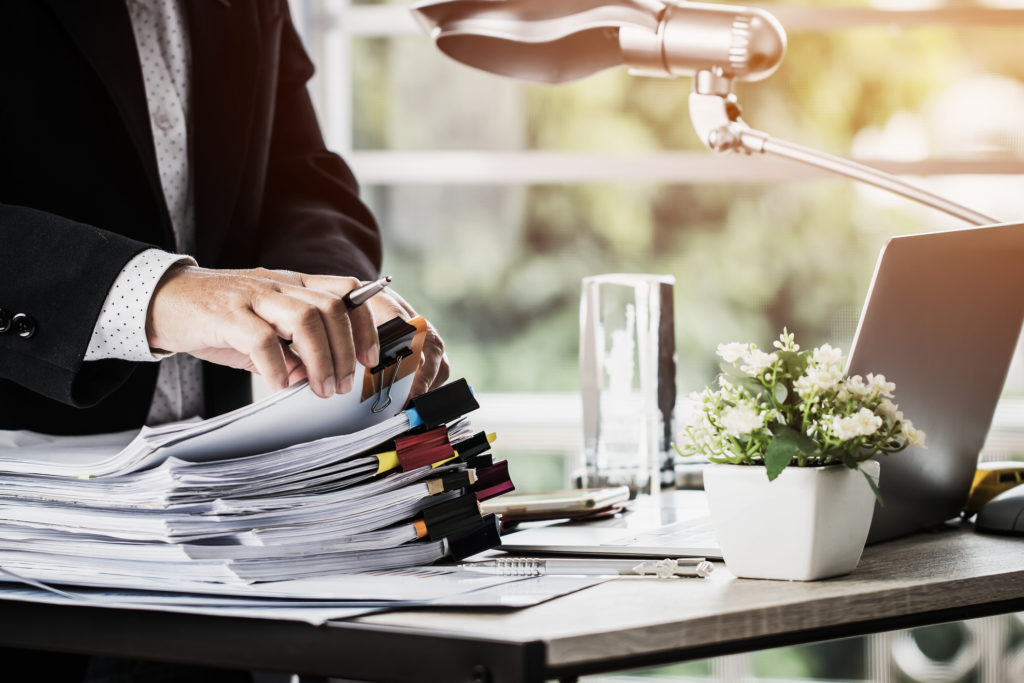 Business professional reviewing a large stack of documents at an office desk